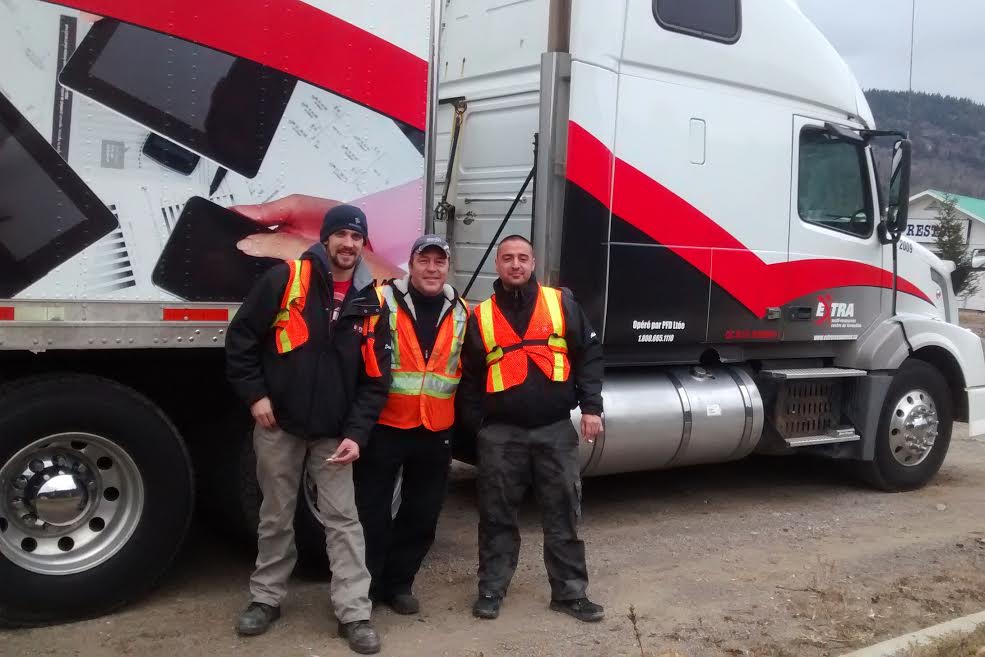 Trois camionneurs avec des dossards oranges devant un camion